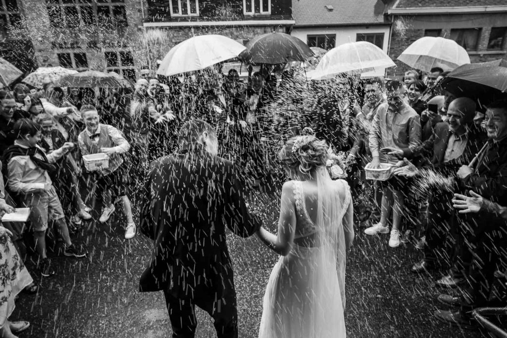 Sortie de cérémonie sous la pluie avec des parapluies blancs, en noir et blanc