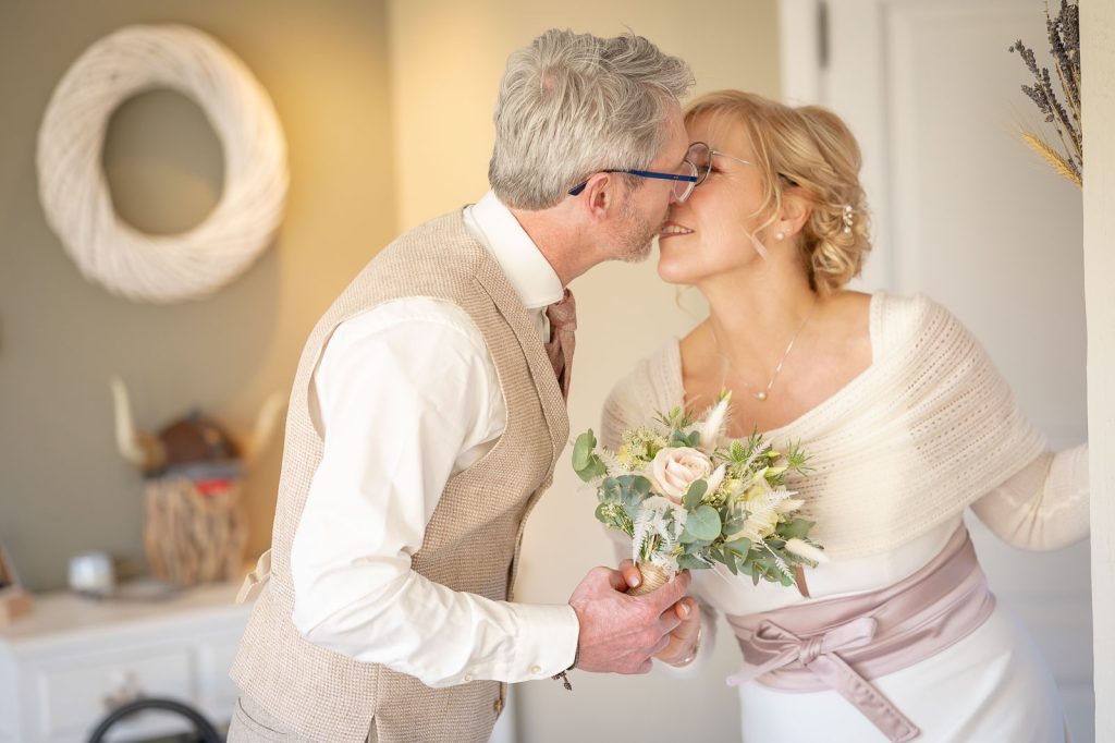 Le marié embrasse la mariée sur la joue, bouquet à la main