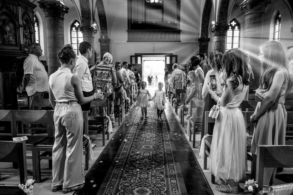 Sortie des mariés dans l'allée d'une église, invités debout, en noir et blanc