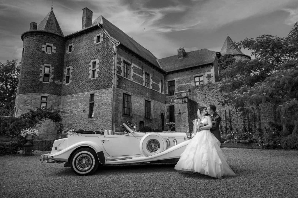 La mariée près d'une voiture blanche de collection devant un château, en noir et blanc