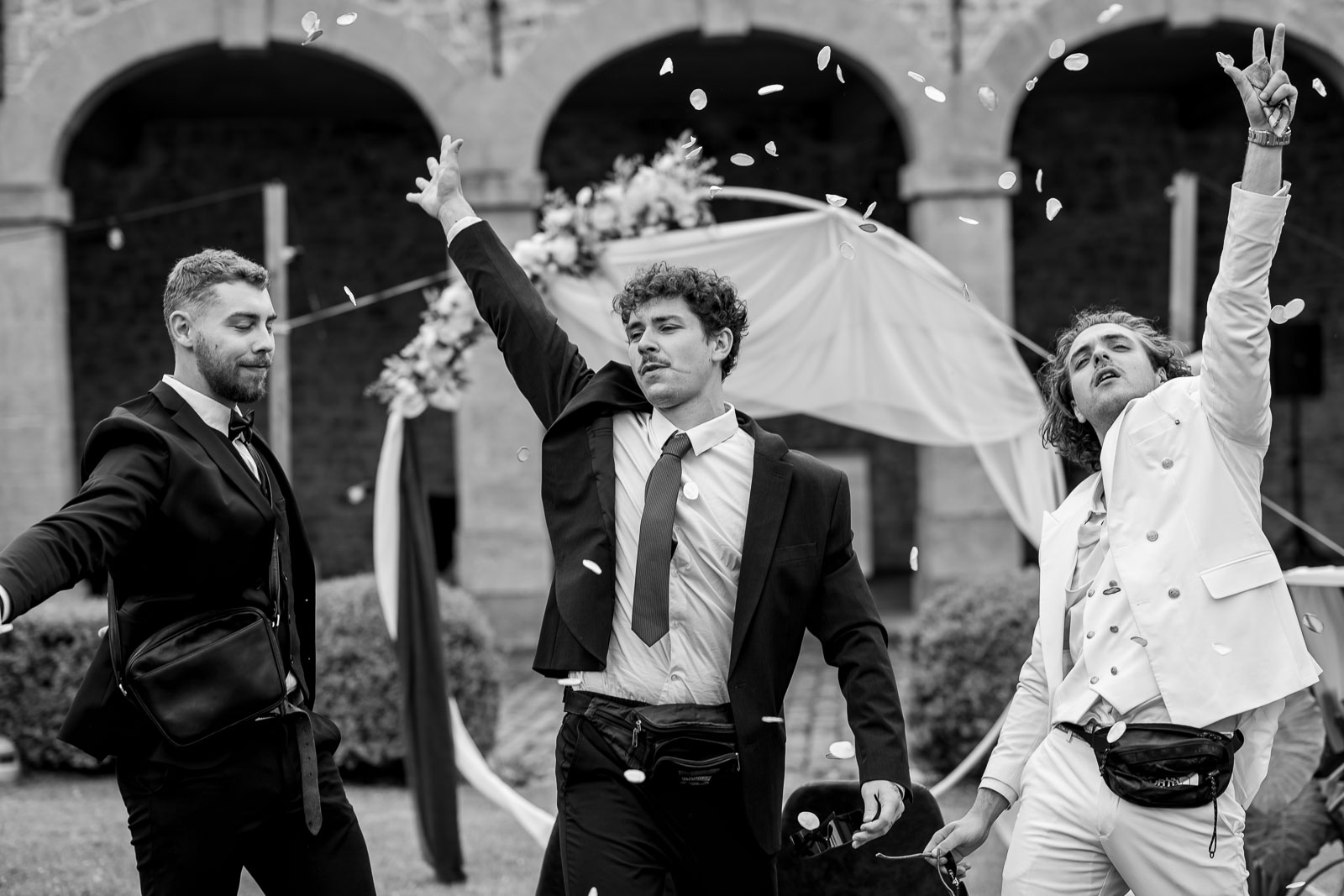 Les invités lancent des confettis sur les mariés sous les arcades, en noir et blanc