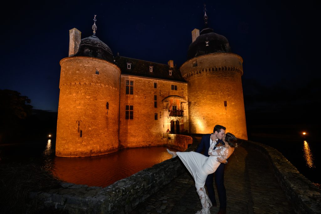 Les mariés s'embrassent de nuit devant le Château de Lavaux-Sainte-Anne illuminé
